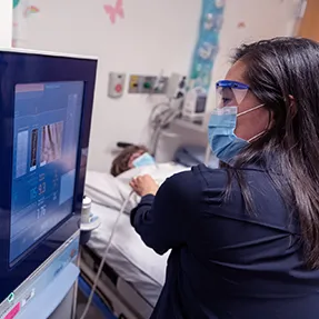 Clinician looks at imagery before working with patient laying in hospital bed.