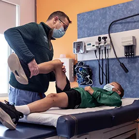 Clinician bends young male patient's leg as boy lay on exam room table
