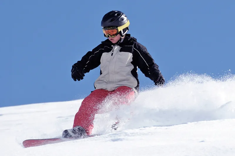 A person wearing ski gear snowboards down a hill