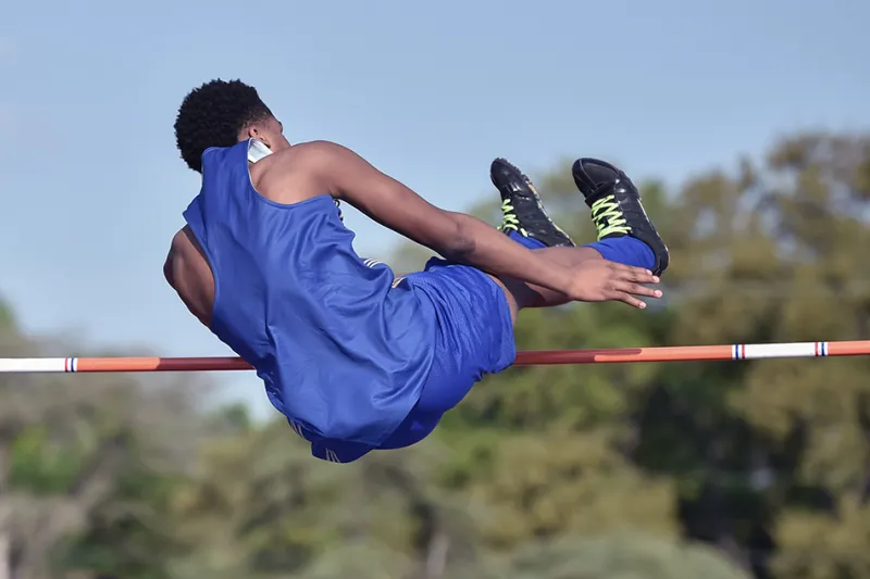 Male athlete in air jumps over bar during the high jump