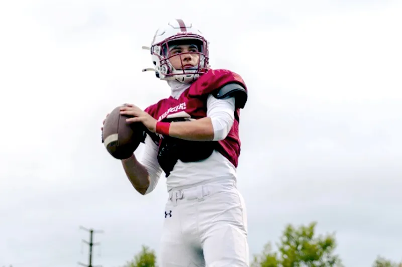 Quarterback wears helmet, prepares to throw pass with right hand, left hand holds onto football