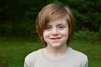 Tween boy with hair parted to the right poses for photo in a wooded area.