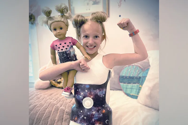 Young girl holds doll while doing Rosie the Riveter pose