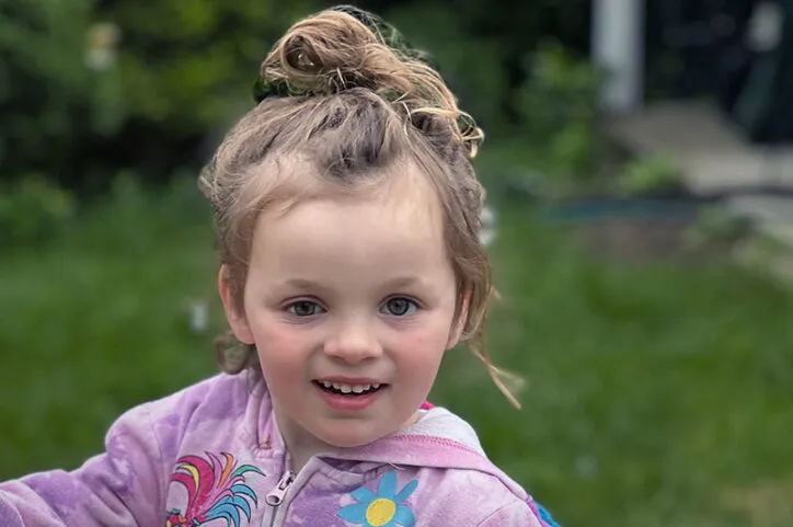 Young girl wearing pink jacket and with hair in bun poses for cameras outdoors