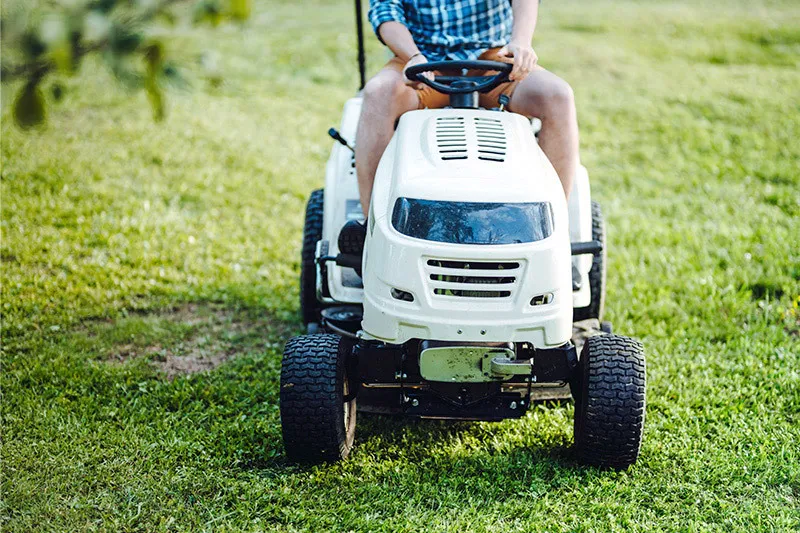 Person wearing shorts uses riding lawnmower
