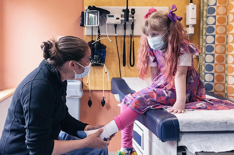 Clinician examines ankle of child who is sitting on exam room table