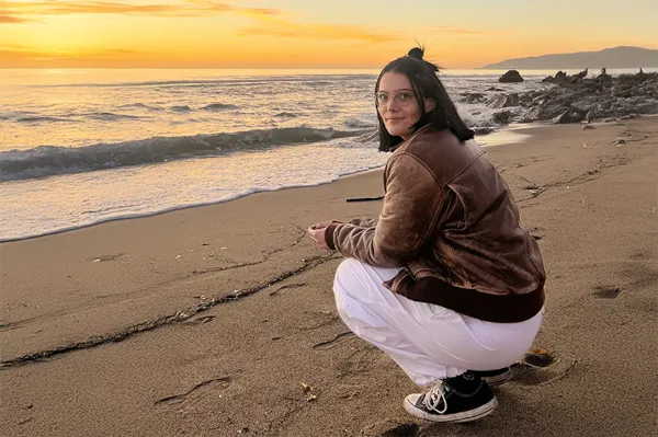 Young woman squats while water crashes into beach