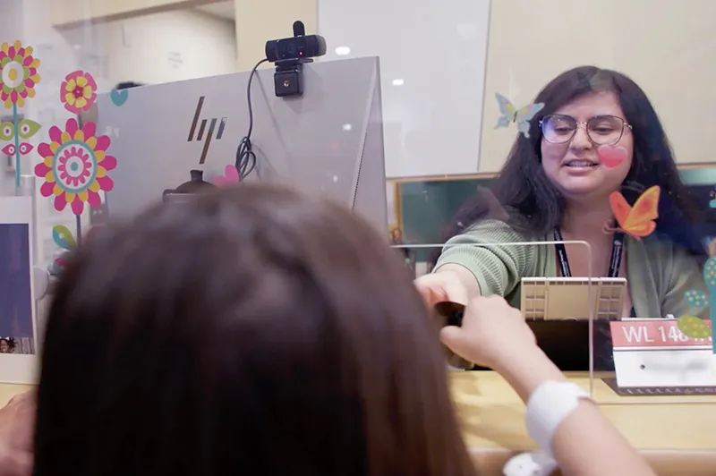 A woman at a counter hands a pair of sunglasses to a little girl.