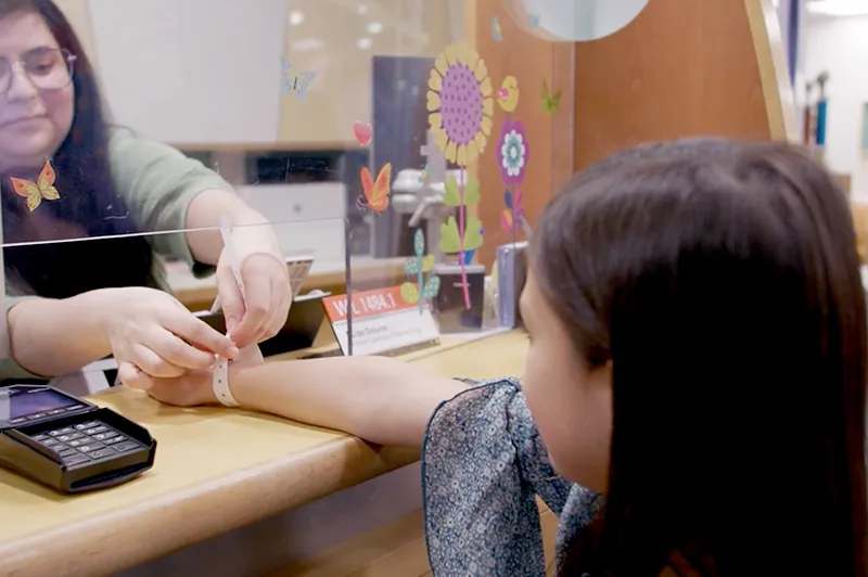 A woman putting a wristband on a child from behind a check-in counter.