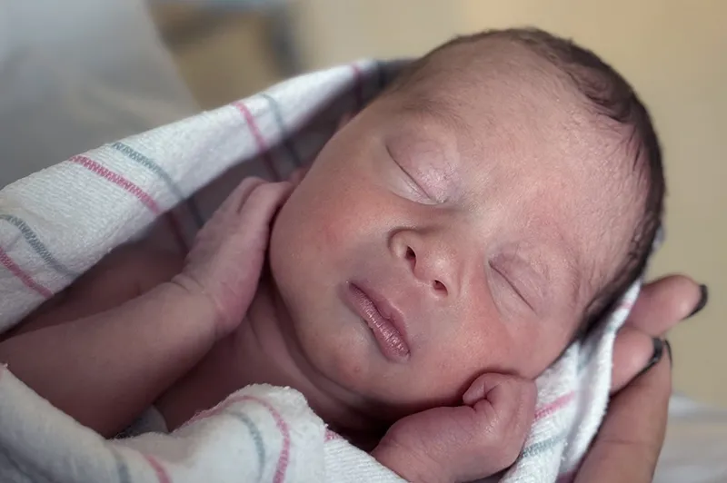 Baby swaddled in blanket, being held in adult's hands