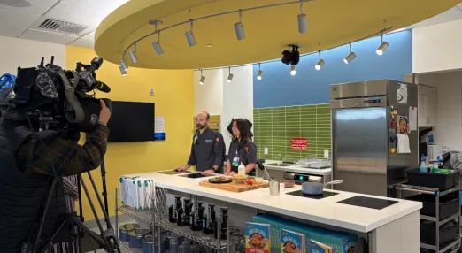 Camera crew films two adults standing behind kitchen island