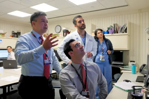 Four people gather together and appear to be looking up at a monitor
