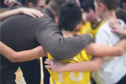 Players and coach gather together in huddle, arms around each other