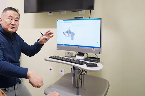 Male clinician gestures at monitor showing imagery of a hip