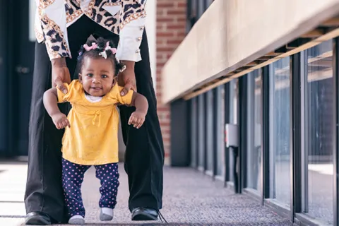Adult holds up toddler as she starts to walk down corridor